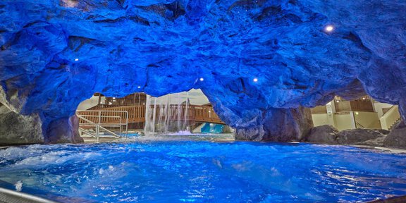 A blue swimming pool set in a rocky landscape with gentle waterfalls. The lighting creates a relaxing atmosphere. - Erlebnishallenbad Freizeit Arena - Sölden