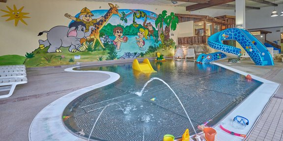 An indoor pool with colorful murals of animals and a cheerful landscape. There is a slide, water fountains, and toys in the water. - Erlebnishallenbad Freizeit Arena - Sölden