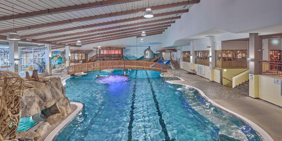An indoor water park with a large, blue pool and various slides. The environment is brightly lit and has a friendly atmosphere. - Erlebnishallenbad Freizeit Arena - Sölden