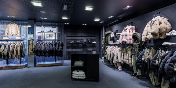 Ein moderner Bekleidungsladen mit verschiedenen Jacken und Mänteln an den Wänden. Der Raum ist gut beleuchtet und hat einen eleganten, minimalistischen Stil. - Sport4You Filiale Avenzio - Sölden