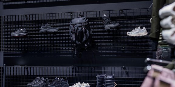 Ein modernes Schuhregal mit verschiedenen Sportschuhen und einem Rucksack. Die Produkte sind in einem eleganten, minimalistischen Design präsentiert. - Sport4You Filiale Avenzio - Sölden