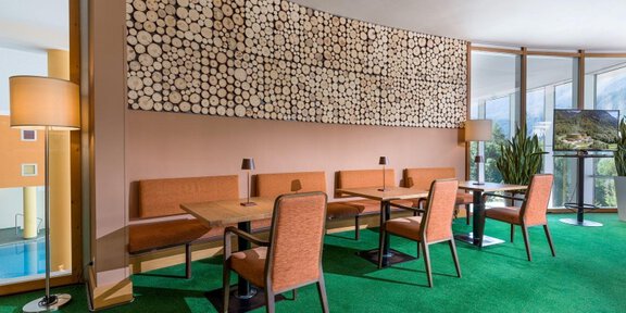A modern interior with wooden decor and cozy seating areas. The carpet is green and there are large windows that let in plenty of light. - Café-Hotelbar im Vivea 4*Hotel Umhausen im Ötztal - Umhausen