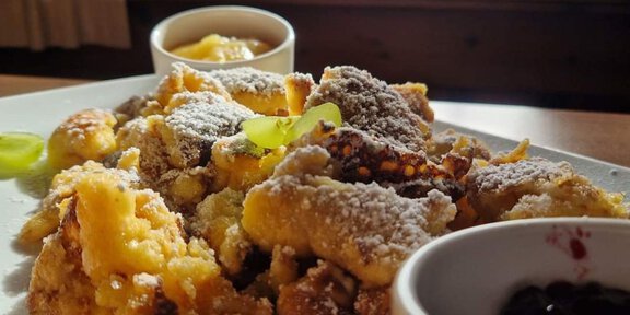 A plate of Kaiserschmarrn, dusted with powdered sugar, served with applesauce and jam. Snow-covered mountains are visible in the background. - Hochjoch Hospiz - Vent