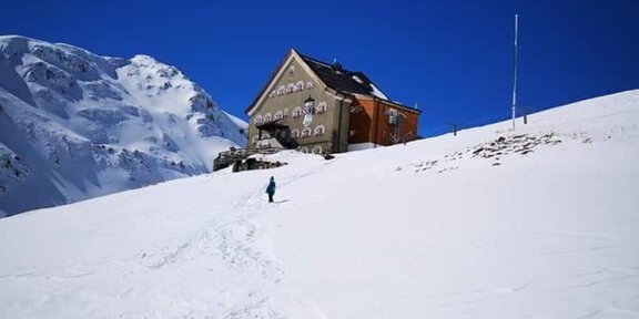A snowy landscape with a house in the background. The sky is clear and blue. - Hochjoch Hospiz - Vent