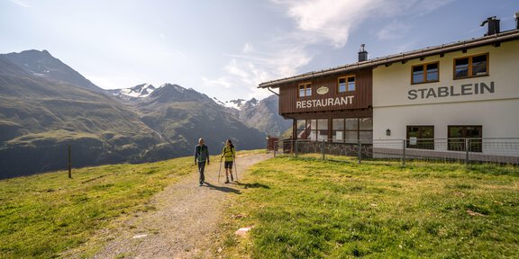 Ein schöner Wanderweg führt zu einem Restaurant in den Bergen. Im Hintergrund sind majestätische Berge und ein blauer Himmel zu sehen. - 6er Sesselbahn Wildes Mannle - Vent