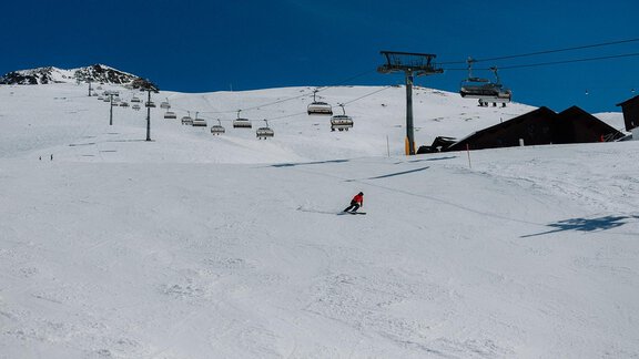 Ein Skifahrer fährt die verschneite Piste hinunter. Im Hintergrund sind Seilbahnen und ein klarer blauer Himmel zu sehen. - TOP Hotel Hochgurgl - Hochgurgl