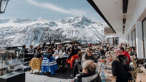 Eine belebte Terrasse mit Menschen, die die Aussicht auf schneebedeckte Berge genießen. Die Besucher sitzen an Tischen und scheinen eine entspannte Zeit zu haben. - TOP Hotel Hochgurgl - Hochgurgl