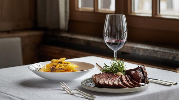 Ein eleganter Tisch mit einem Teller Fleisch und einer Schüssel Pasta. Ein Glas Rotwein ergänzt das ansprechende Setting. - TOP Hotel Hochgurgl - Hochgurgl