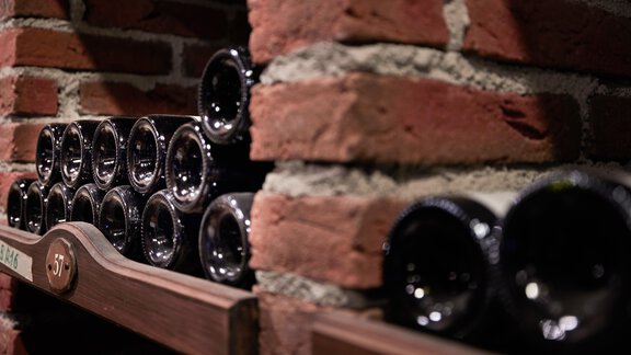 Eine elegante Weinregal mit mehreren schwarzen Weinflaschen. Die Flaschen sind an einer Ziegelwand aufgereiht. - TOP Hotel Hochgurgl - Hochgurgl