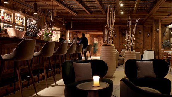 Eine stilvolle Bar mit eleganten Stühlen und einer warmen Atmosphäre. Kerzenlicht und dekorative Pflanzen schaffen eine einladende Umgebung. - TOP Hotel Hochgurgl - Hochgurgl