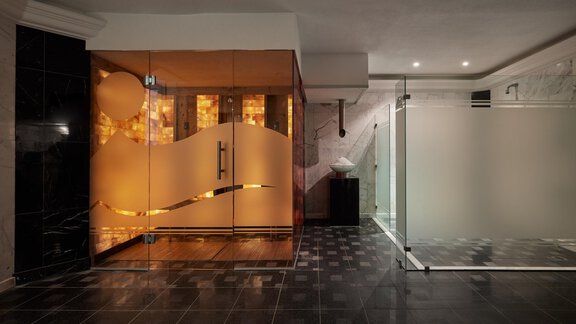 Ein moderner Wellnessbereich mit einer Glas-Sauna und einer transparenten Duschkabine. Der Boden ist mit dunklen Fliesen ausgelegt und die Beleuchtung schafft eine entspannende Atmosphäre. - TOP Hotel Hochgurgl - Hochgurgl
