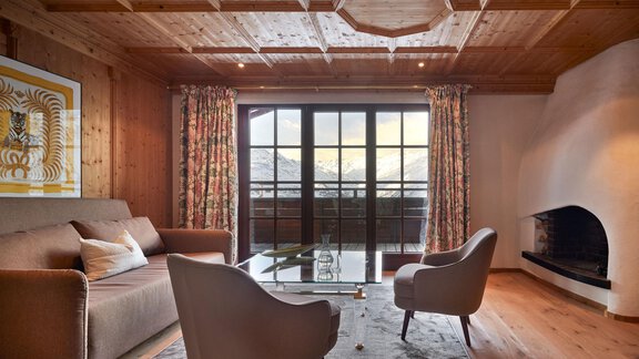 Ein gemütliches Wohnzimmer mit Holzverkleidung und großen Fenstern. Die Einrichtung besteht aus einem Sofa und zwei Stühlen, mit Blick auf die Berge. - TOP Hotel Hochgurgl - Hochgurgl