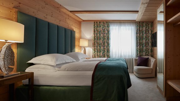Ein elegantes Hotelzimmer mit einem großen Bett und einem gemütlichen Sessel. Die Holzwände und die stilvollen Vorhänge sorgen für eine warme Atmosphäre. - TOP Hotel Hochgurgl - Hochgurgl