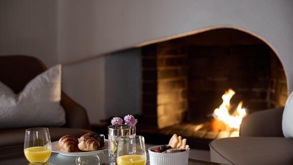 Ein gemütliches Wohnzimmer mit einem offenen Kamin. Auf dem Tisch stehen Gläser mit Orangensaft, Gebäck und frische Früchte. - TOP Hotel Hochgurgl - Hochgurgl