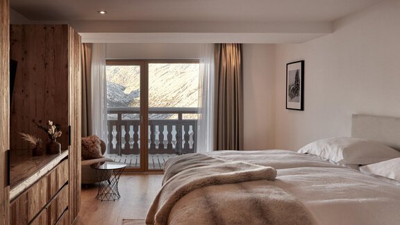 Ein modernes Schlafzimmer mit einem großen Fenster, das auf einen Balkon blickt. Die Einrichtung ist gemütlich mit einem Holzschrank und einer warmen Decke auf dem Bett. - TOP Hotel Hochgurgl - Hochgurgl