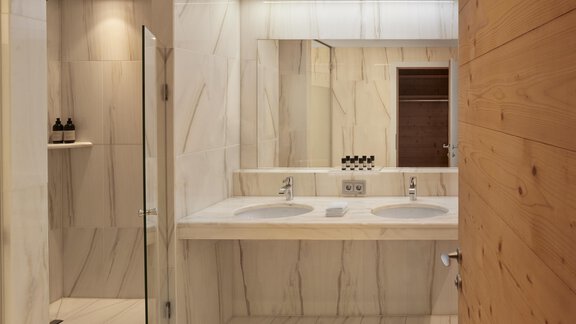 Ein modernes Badezimmer mit marmorierten Wänden und zwei Waschbecken. Es gibt einen großen Spiegel und eine elegante Holzverkleidung. - TOP Hotel Hochgurgl - Hochgurgl