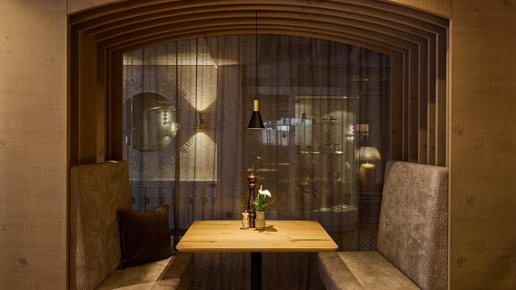 A cozy dining area with wood paneling and soft seating. A small table with a floral decoration and gentle lighting creates an inviting atmosphere. - Art & Relax Hotel Bergwelt - Obergurgl 