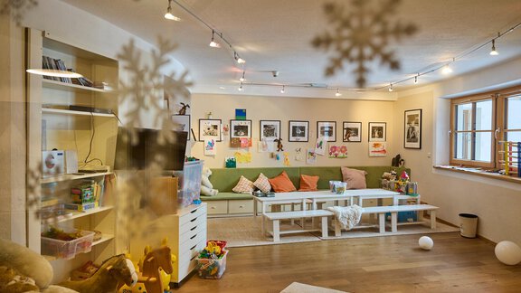 A cozy room with a bright couch and many cushions. Pictures hang on the walls and there are child-friendly toys. - Art & Relax Hotel Bergwelt - Obergurgl 