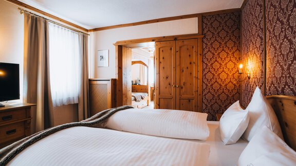 A cozy bedroom with two single beds and wooden decor. A television and a bright window front create an inviting atmosphere. - Art & Relax Hotel Bergwelt - Obergurgl 