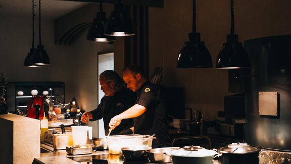 Two chefs are working in a modern kitchen. They are preparing various dishes in a well-lit space. - Art & Relax Hotel Bergwelt - Obergurgl 