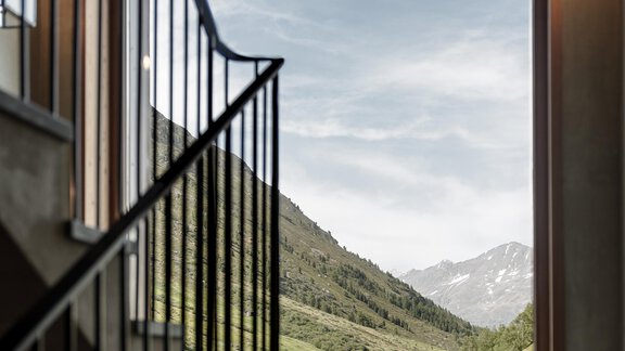A window overlooking green hills and mountains. The sky is clear and the passage has a modern staircase. - Chalet Cecilia by MYALPS - Obergurgl 