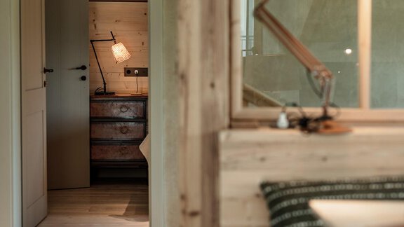 A cozy room with wooden walls and a large window. In the background, a desk with a lamp and another door is visible. - Chalet Cecilia by MYALPS - Obergurgl 
