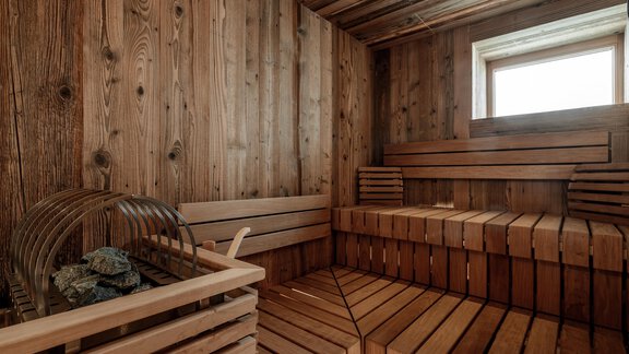 A cozy sauna area with wooden shelves and a window opening. The walls are made of light wood, and the space radiates warmth and relaxation. - Chalet Cecilia by MYALPS - Obergurgl 