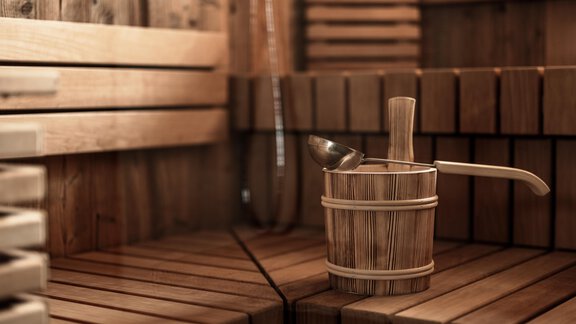 A cozy sauna with wooden paneling and benches. In the center stands a wooden container with a ladle. - Chalet Cecilia by MYALPS - Obergurgl 