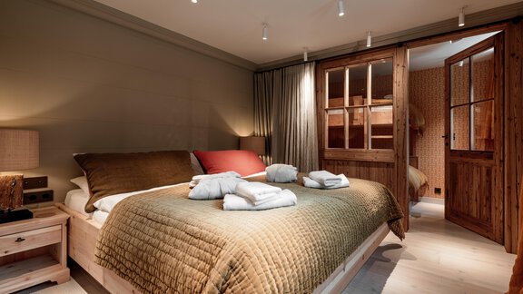 A stylish bedroom with a large bed and cozy bedding. The walls are in warm colors and there is access to another room. - Chalet Cecilia by MYALPS - Obergurgl 
