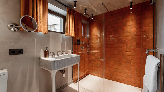 A modern bathroom with a glass shower and orange curtains. The walls are covered with brown tiles, and an elegant sink is present. - Chalet Cecilia by MYALPS - Obergurgl 