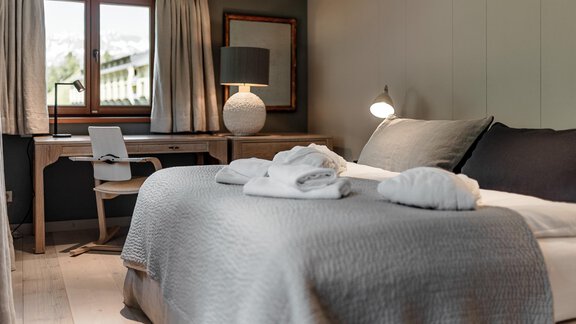 A cozy bedroom with a large bed and soft towels. The room has a relaxing atmosphere and is furnished with a desk and a lamp. - Chalet Cecilia by MYALPS - Obergurgl 