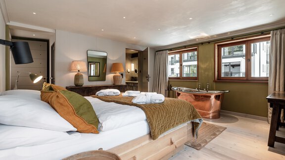 A modern bedroom with a comfortable bed and warm colors. In the background, a bathtub and natural light sources can be seen. - Chalet Cecilia by MYALPS - Obergurgl 