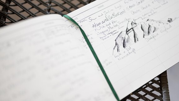 An open notebook with handwritten notes and a sketch of mountains. The book is lying on a grid table. - Chalet Cecilia by MYALPS - Obergurgl 