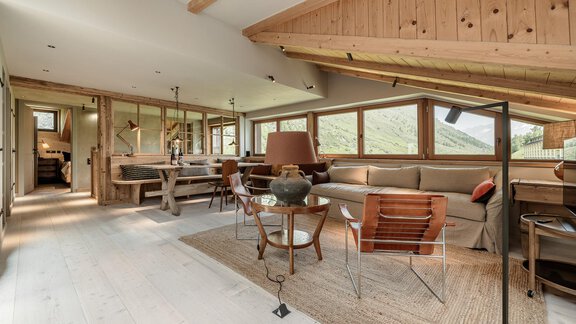 A modern living atmosphere with wooden ceilings and large windows. The room is bright and inviting, featuring a cozy sofa and stylish furniture. - Chalet Cecilia by MYALPS - Obergurgl 