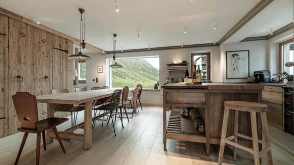 A modern kitchen with wood surfaces and a large dining table. Large windows provide a view of the surrounding landscape. - Chalet Cecilia by MYALPS - Obergurgl 