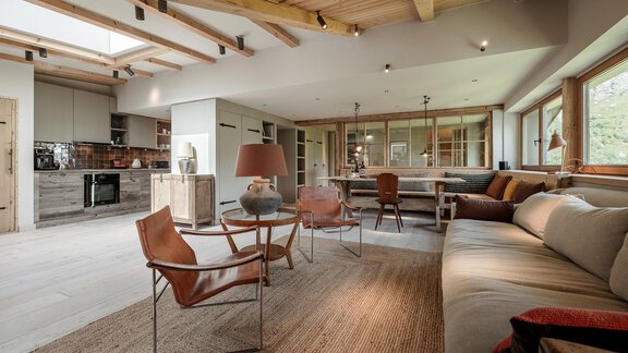 A modern living room with wooden beams and large windows. The decor is stylish and cozy, featuring a sofa and a round table. - Chalet Cecilia by MYALPS - Obergurgl 