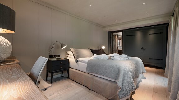 A modern bedroom with a large bed and a neutral color tone. In the corner, there is a nightstand and a floor lamp that creates a cozy atmosphere. - Chalet Cecilia by MYALPS - Obergurgl 