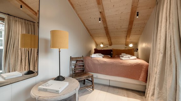 A cozy bedroom with a wooden ceiling and soft lighting. The room is furnished with a bed, a chair, and a table. - Chalet Cecilia by MYALPS - Obergurgl 