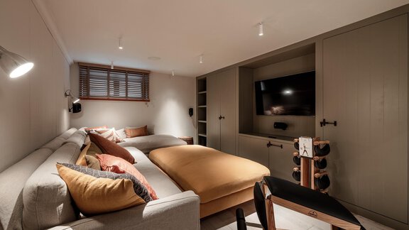 A cozy room with a sofa bed and a large bed. There's a television on the wall and warm light from the ceiling. - Chalet Cecilia by MYALPS - Obergurgl 