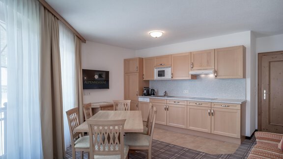 A modern kitchenette with wooden cabinets and a dining area. Large windows let in a lot of light. - Ferienwohnung de Luxe Alpenresidenz am Mühlbach - Obergurgl 