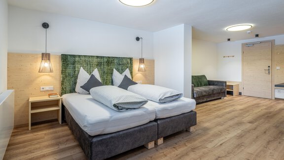 A modern hotel room with two single beds and a cozy seating area. The walls are in neutral colors and there are soothing wood details. - Haus Gstrein - Obergurgl 