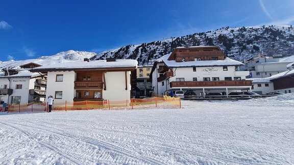 A winter landscape with snow-covered buildings. In the background, there are mountains under a clear blue sky. - Haus Mennecke - Obergurgl 