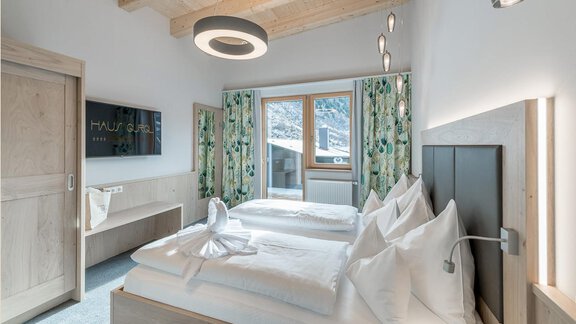 Ein modernes Schlafzimmer mit zwei Betten und eleganten Holzdetails. Große Fenster lassen viel Licht herein und bieten einen Blick auf die Umgebung. - Skihotel Haus Gurgl - Obergurgl 