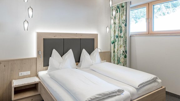 Ein gemütliches Schlafzimmer mit zwei getrennten Betten und modernen Holzdetails. Die Fenster lassen viel Tageslicht hereinkommen und die Vorhänge sorgen für eine angenehme Atmosphäre. - Skihotel Haus Gurgl - Obergurgl 