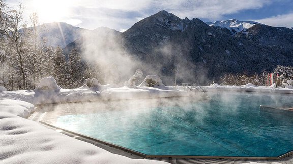 A heated outdoor pool in a snowy landscape. In the background, majestic mountains can be seen under a clear sky. - Vivea 4* Hotel Umhausen im Ötztal - Umhausen