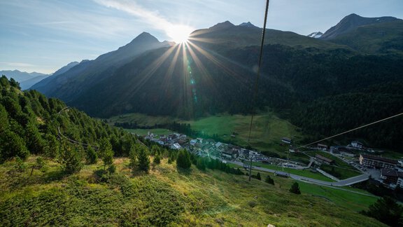 A beautiful mountain landscape with a radiant sunrise. In the foreground, there are green meadows and trees, while the mountains rise in the background. - Hotel Alt Vent - Tyrol - Vent