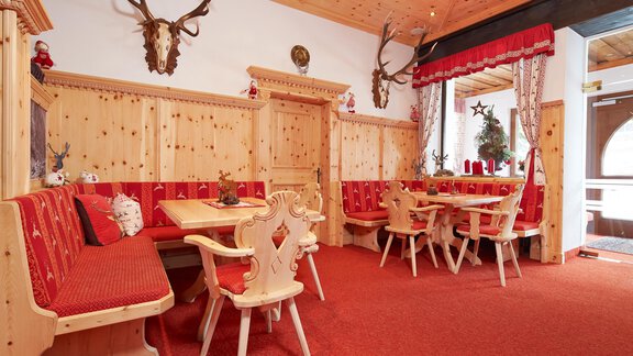 A cozy dining area with wooden paneling and red seat cushions. Antler remains hang on the walls, and the room is brightly lit. - Hotel Vent - Vent