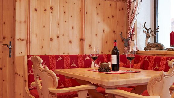 A cozy dining area with wooden walls and a red bench. On the table are a wine bottle and glasses. - Hotel Vent - Vent