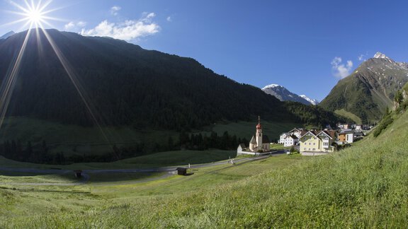 A picturesque mountain landscape with a small village and a church. In the background, high mountains and a clear blue sky can be seen. - Hotel Vent - Vent