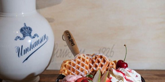 Ein leckerer Eisbecher mit Sahne, frischen Früchten und Waffeln. Im Hintergrund steht eine dekorative Kanne. - ÖTZTALEREI Café-Burgerbar-Eiswerkstatt - Umhausen